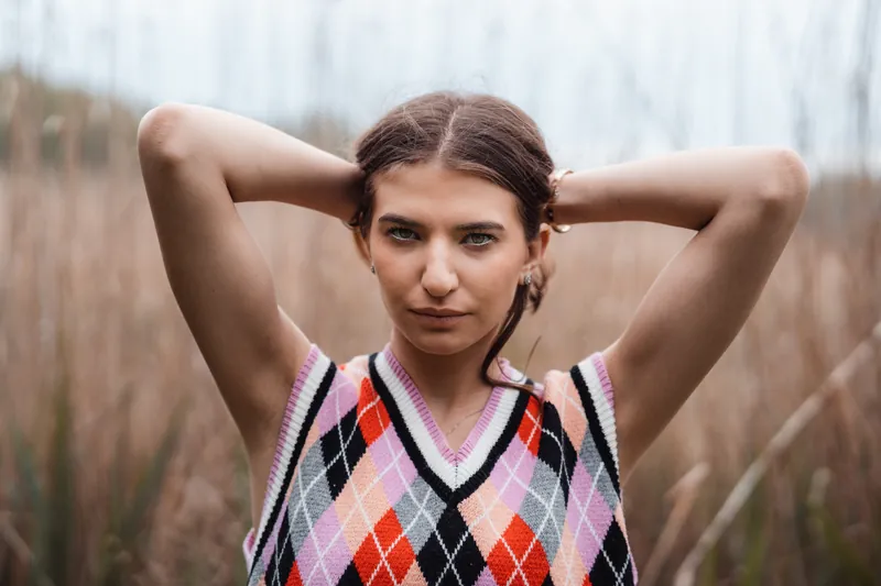 Model in an argyle knit vest among tall reeds, overcast light