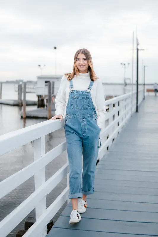 Denim overalls and a white turtleneck on a wooden pier