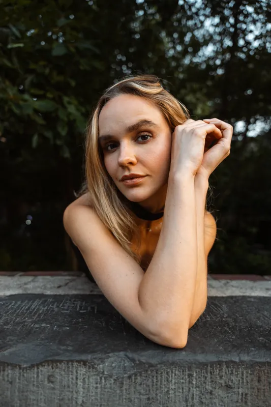 Close portrait leaning on a stone ledge, dark greenery behind