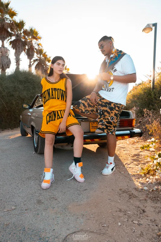 Two models in streetwear by a gold vintage Mercedes on a palm lined road, Israel