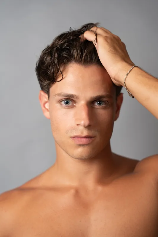 Close headshot, hand in hair, grey studio backdrop