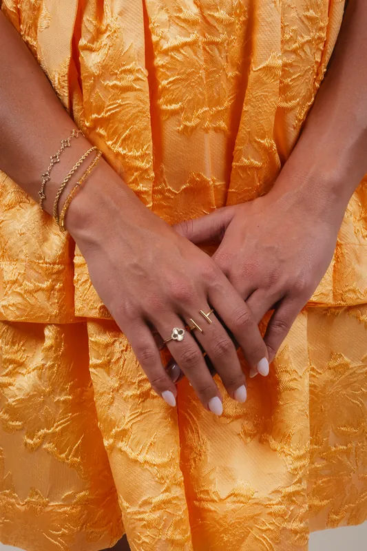 Gold rings and bracelets on hands over an orange jacquard dress