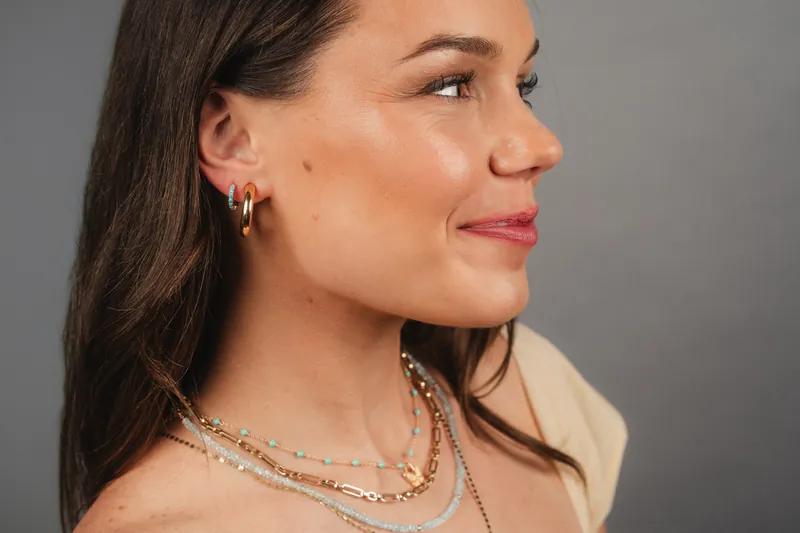 Layered gold and turquoise bead necklaces with gold hoops, grey backdrop