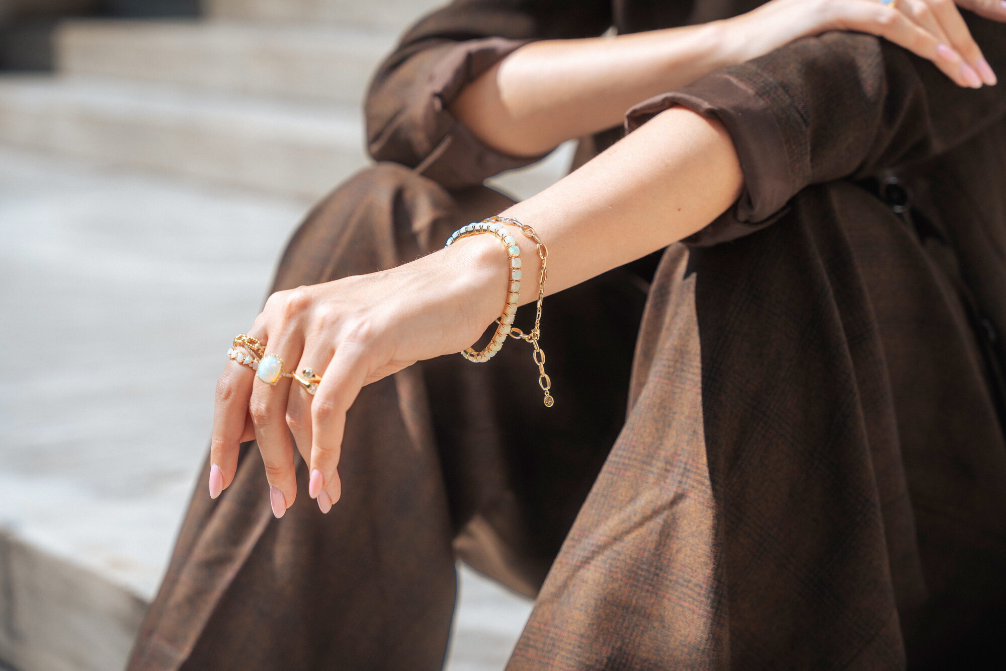 Close-up of EFFY gold bracelets and rings on a model seated on stone steps